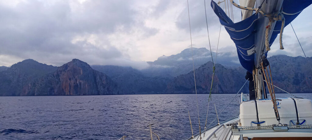 Stunning aerial view of the Tramuntana Mountains in Mallorca, showcasing rugged peaks and lush valleys extending towards a serene seafront under blue sky.